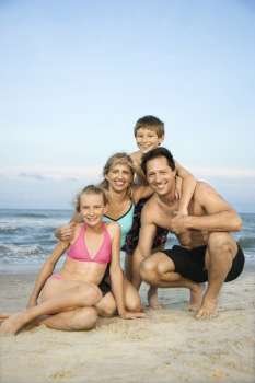 Caucasian family of four posing together on beach.