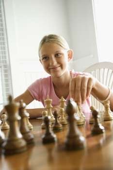 Caucasian pre-teen girl playing chess smiling.