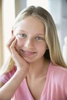 Portrait of Caucasian pre-teen girl looking at viewer resting chin in hand and smiling.