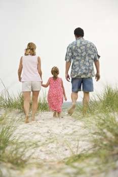 Caucasian mid-adult man and woman walking with female child toward beach.