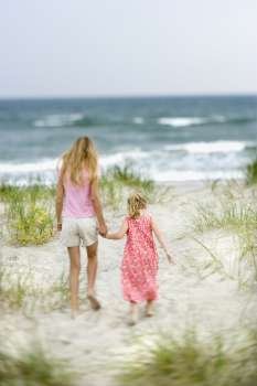 Caucasian pre-teen girl holding hands with younger Caucasian girl walking toward beach.