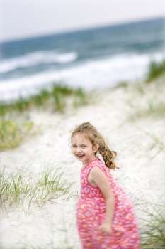 Caucasian female child on beach turning around looking at viewer smiling.