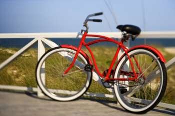 Red beach cruiser bicycle leaning against walkway rail on beach on Bald Head Island, North Carolina.