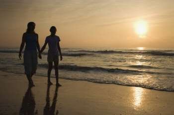 Caucasian prime adult female and female child walking on beach at sunset holding hands.