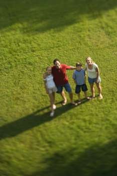 Caucasian family of four standing on lawn with arms around each other.