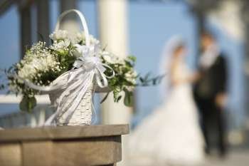 Flower basket with Caucasian bride and groom blurred in background.