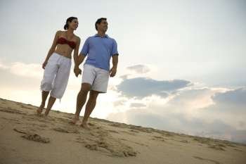 Caucasian mid-adult couple holding hands walking on beach.