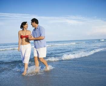 Caucasian mid-adult couple holding hands wading in ocean.