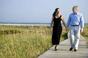 Caucasian mid-adult couple holding hands and walking on walkway.