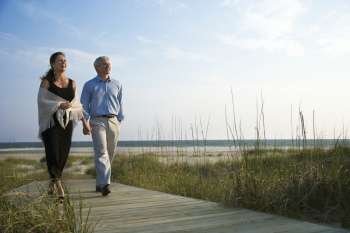 Caucasian mid-adult couple holding hands and walking down walkway at beach.