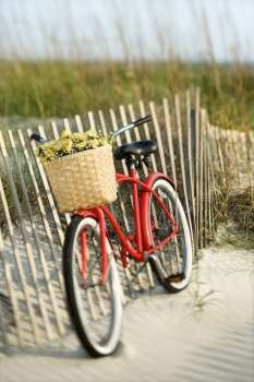 Red vintage bicycle with basket and flowers leaning against wooden fence at beach.