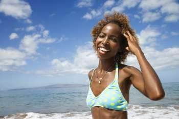 Mid-adult African American female smiling and touhing hair with ocean in background.