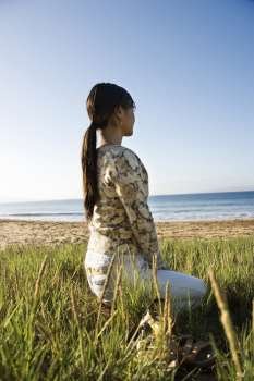 Young Asian female sitting on beach looking out to ocean.