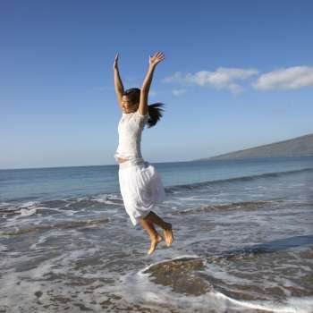 Young Asian female jumping in air at the shoreline.