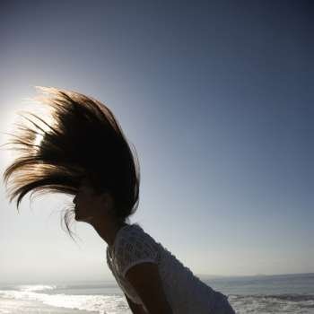 Young Asian female swinging her hair back at the beach with sun in background.