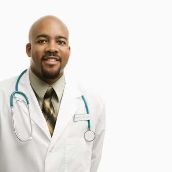Portrait of smiling African-American man doctor wearing uniform standing against white background.