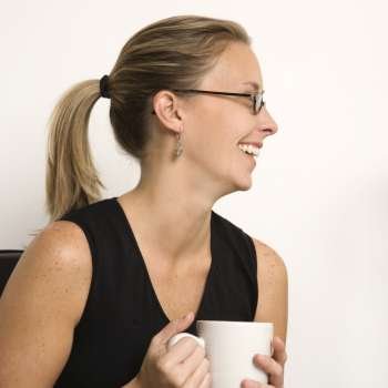 Caucasian mid-adult woman wearing eyeglasses holding coffee cup and looking to side.