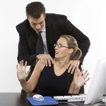 Caucasian mid-adult man sexually harassing woman sitting at computer.