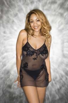 Portrait of pretty smiling woman standing against silver background in sheer black lingerie.