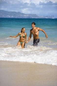 Attractive couple embracing and smiling as they walk out of water in Maui, Hawaii.
