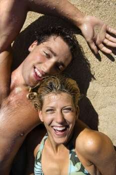 Smiling happy couple lying in sand on Maui, Hawaii beach.