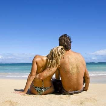 Rear view of couple sitting on Maui, Hawaii beach with woman leaning head on man´s shoulder.