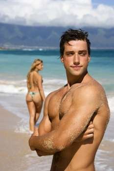 Handsome man standing on Maui, Hawaii beach with woman in background.