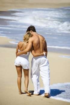 Attractive couple walking on Maui, Hawaii beach with arms around eachother.