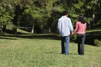 Couple holding hands walking and talking in park.