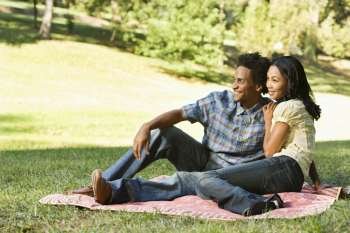 Portrait of attractive smiling couple in park sitting on picnic blanket.