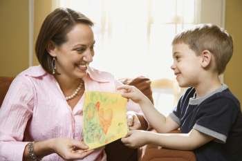 Caucasian boy giving mid adult mother a drawing.