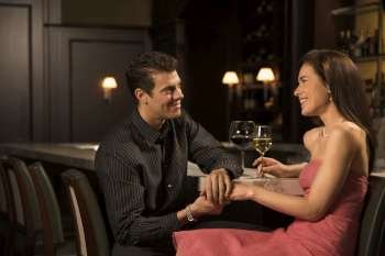 Mid adult Caucasian couple at bar holding hands and smiling.