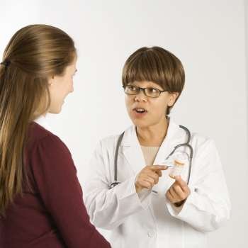 African American middle-aged female doctor explaining medication to Caucasian mid-adult female patient.