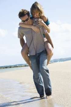Mid-adult Caucasian man giving woman piggyback ride on beach.