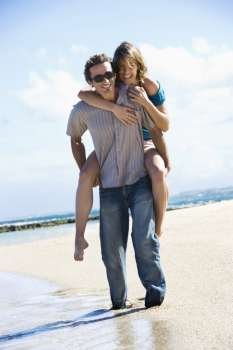 Mid-adult Caucasian man giving woman piggyback ride on beach.