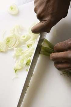 African-American male hands using large kitchen knife to chop fennel.