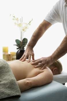 Caucasian middle-aged male massage therapist massaging back of Caucasian middle-aged woman lying on massage table.
