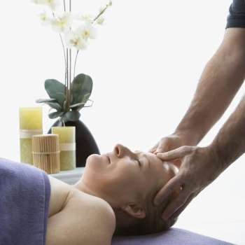 Caucasian middle-aged male massage therapist massaging temples of Caucasian middle-aged woman lying on massage table.