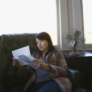 Pretty young Asian woman sitting in green chair reading letter.
