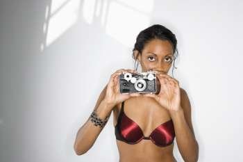 Mid-adult African American woman in bra holding up camera looking at viewer.