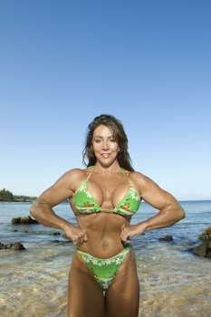 Pretty Caucasian mid adult woman bodybuilder in bikini flexing muscles on Maui beach.