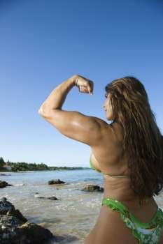 Pretty Caucasian mid adult woman bodybuilder in bikini flexing bicep on Maui beach.