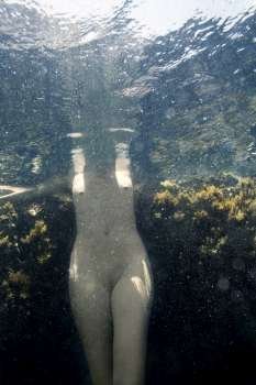 Caucasian young nude female body standing underwater.
