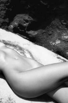 Close up of young Caucasian nude womans midsection lying on rock.