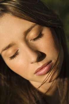 Close-up portrait of attractive young Caucasian woman with eyes closed and long brown hair.