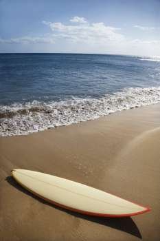 Surfboard on sandy beach with ocean in background in Maui Hawaii.