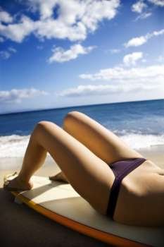Young Caucasian woman in bikini lying on surfboard sunbathing at beach in Maui Hawaii.