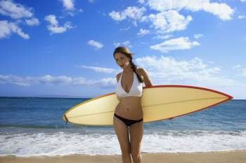 Young pretty Caucasian woman in bikini standing with surfboard at beach in Maui Hawaii.