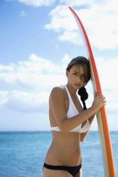 Pretty young Caucasian woman in bikini leaning on surfboard at beach in Maui Hawaii.