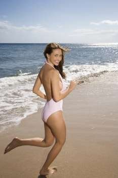 Pretty smiling young Caucasian woman in swimsuit running on beach in Maui Hawaii.